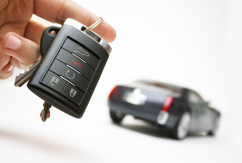 Image of hand holding keys to a new car, with an out of focus car in the background